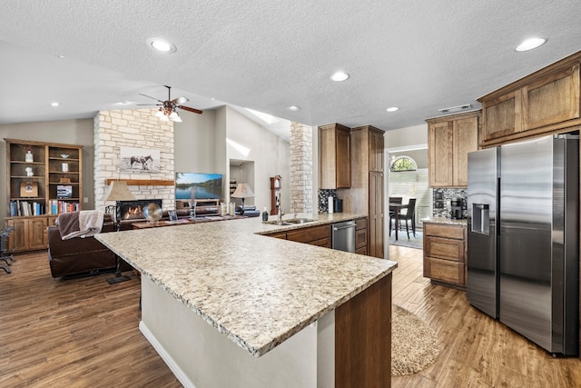 kitchen with lofted ceiling, a stone fireplace, a textured ceiling, hardwood / wood-style flooring, and appliances with stainless steel finishes