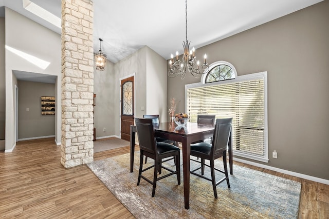 dining area with a high ceiling, wood-type flooring, decorative columns, and a chandelier