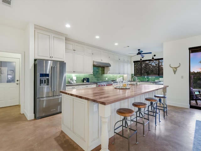 kitchen with ceiling fan, a kitchen breakfast bar, high end refrigerator, a center island with sink, and butcher block counters