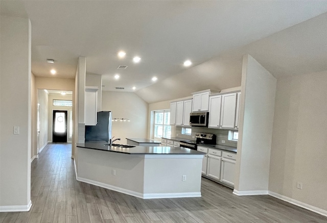 kitchen featuring kitchen peninsula, appliances with stainless steel finishes, light wood-type flooring, vaulted ceiling, and white cabinetry