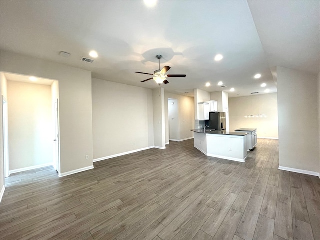 kitchen with ceiling fan, kitchen peninsula, stainless steel fridge, white cabinets, and hardwood / wood-style flooring