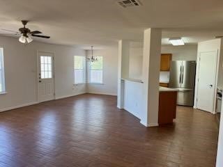 unfurnished living room featuring ceiling fan with notable chandelier and dark wood-type flooring