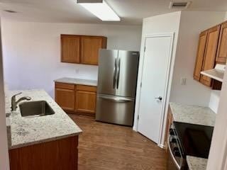 kitchen featuring sink, wood-type flooring, exhaust hood, stainless steel refrigerator, and black range oven