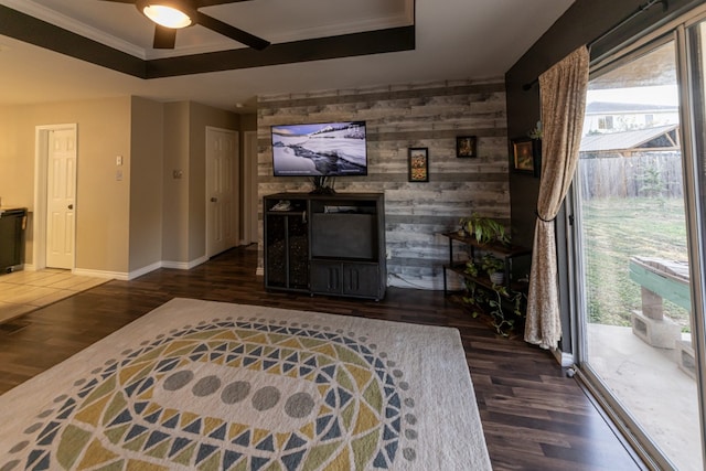 living room with a raised ceiling, ceiling fan, wooden walls, ornamental molding, and dark hardwood / wood-style floors