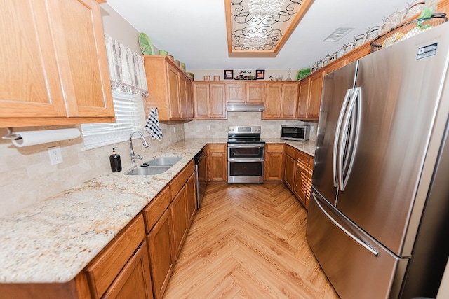 kitchen featuring sink, backsplash, appliances with stainless steel finishes, light stone countertops, and light parquet floors