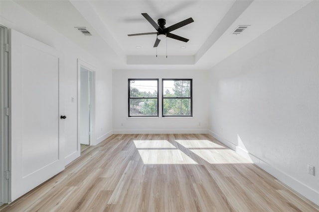 spare room featuring light hardwood / wood-style floors, ceiling fan, and a tray ceiling