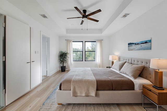 bedroom with light wood-type flooring, a tray ceiling, and ceiling fan