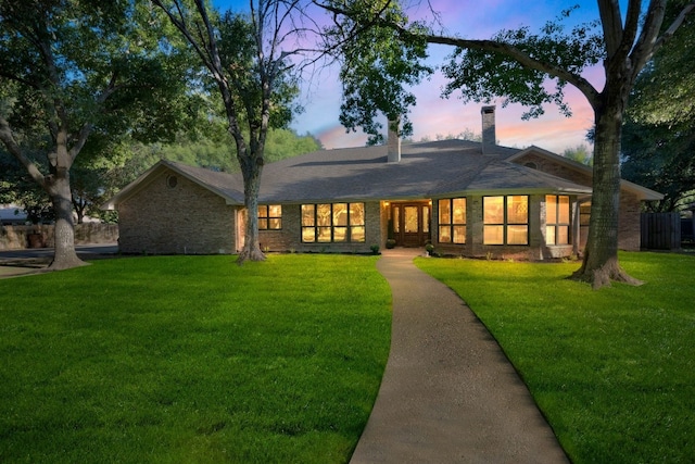 back of property at dusk with a lawn, brick siding, and a chimney