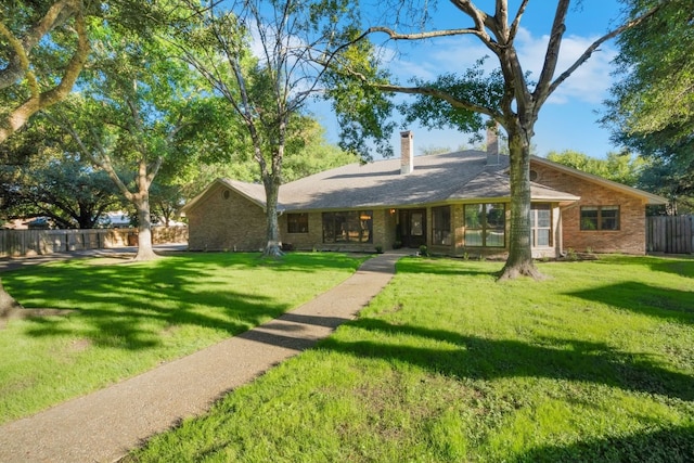 view of front of house featuring brick siding, a chimney, a front lawn, and fence