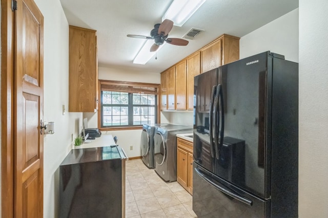 kitchen featuring light tile patterned floors, ceiling fan, black fridge, and washer and dryer