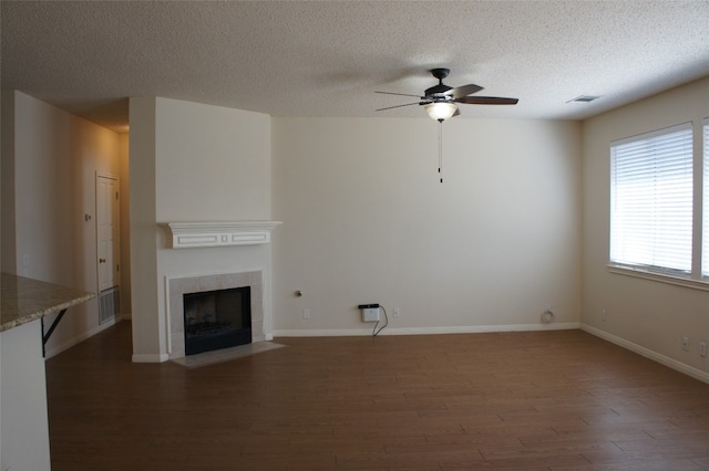 unfurnished living room with ceiling fan, a textured ceiling, a tile fireplace, and dark wood-type flooring