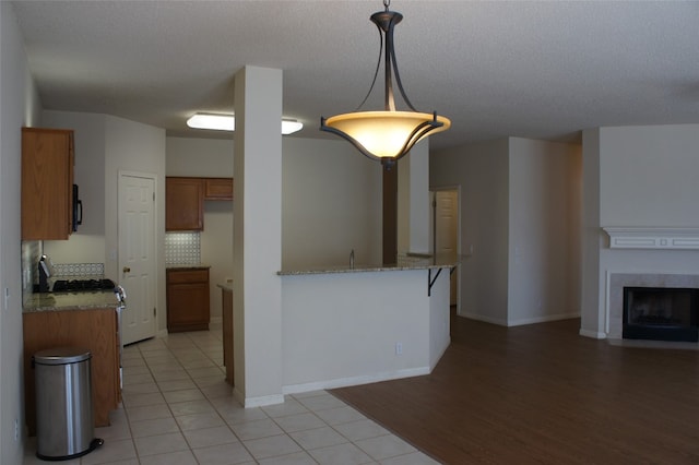 kitchen featuring hanging light fixtures, a fireplace, kitchen peninsula, light stone countertops, and light hardwood / wood-style flooring