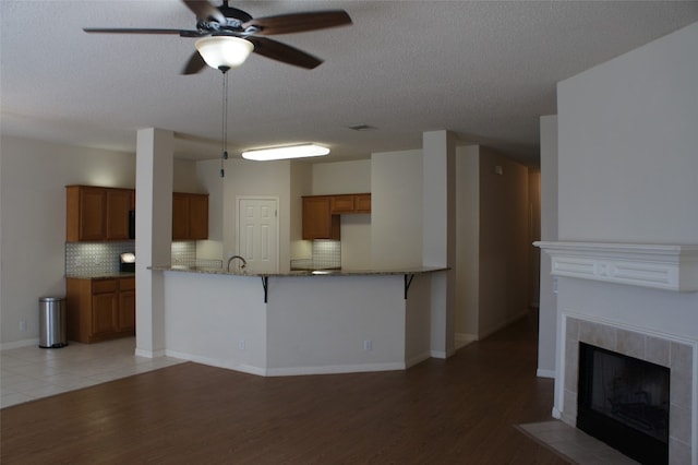 kitchen featuring kitchen peninsula, backsplash, a fireplace, light wood-type flooring, and a kitchen bar