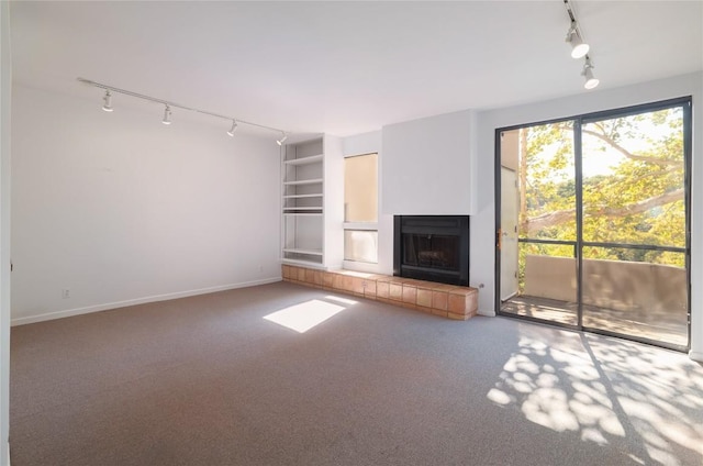 unfurnished living room featuring a tiled fireplace, built in shelves, a healthy amount of sunlight, and rail lighting