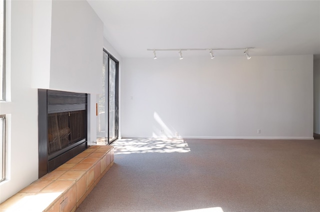 unfurnished living room with track lighting, light colored carpet, and a tile fireplace