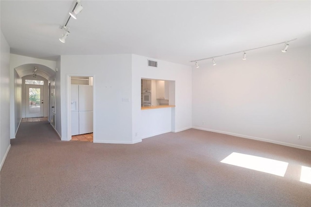 unfurnished living room featuring carpet flooring, track lighting, visible vents, baseboards, and arched walkways