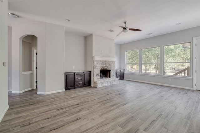 unfurnished living room featuring a stone fireplace, ceiling fan, and light hardwood / wood-style flooring