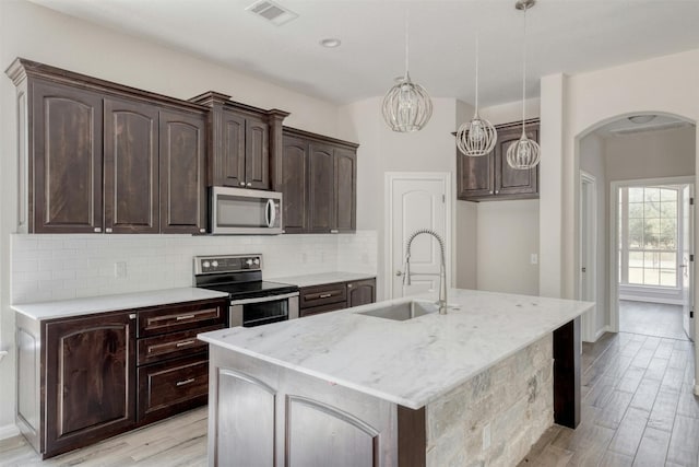 kitchen with appliances with stainless steel finishes, light hardwood / wood-style floors, pendant lighting, and an island with sink