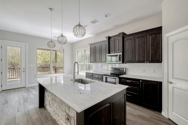 kitchen with pendant lighting, sink, a center island with sink, appliances with stainless steel finishes, and light hardwood / wood-style floors