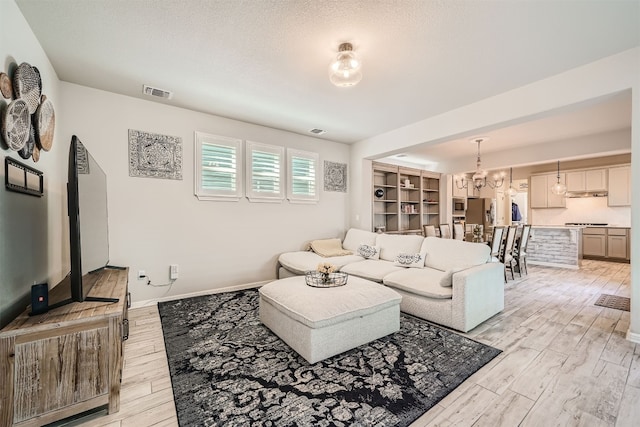 living room featuring an inviting chandelier, light hardwood / wood-style flooring, and a textured ceiling