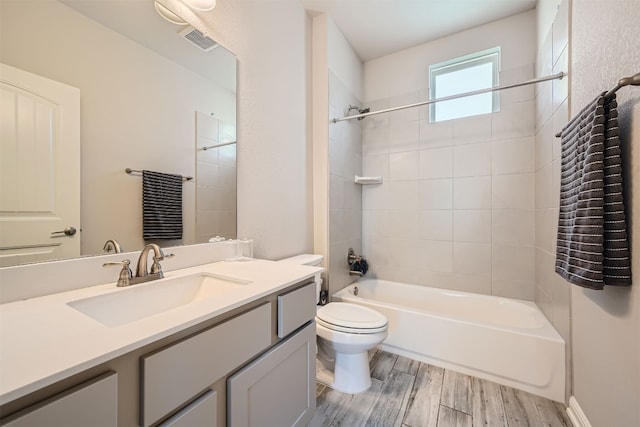 full bathroom with wood-type flooring, tiled shower / bath, vanity, and toilet