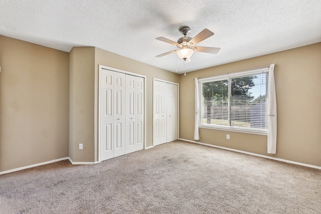 unfurnished bedroom with ceiling fan, carpet floors, two closets, and a textured ceiling