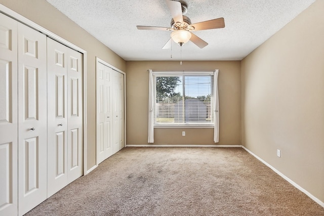 unfurnished bedroom with ceiling fan, light colored carpet, a textured ceiling, and two closets