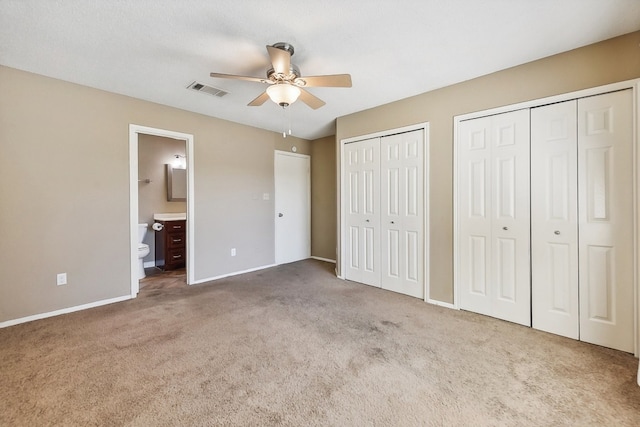 unfurnished bedroom with connected bathroom, two closets, light carpet, and ceiling fan