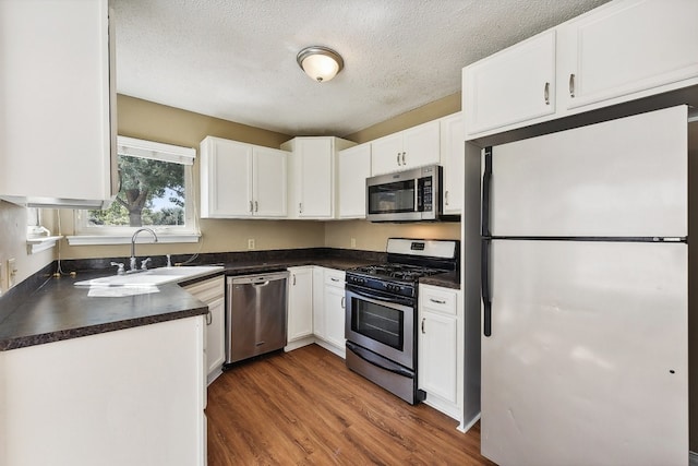 kitchen with appliances with stainless steel finishes, white cabinetry, dark hardwood / wood-style flooring, and sink