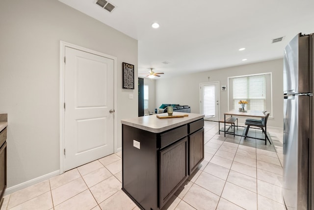 kitchen featuring ceiling fan, dark brown cabinetry, light tile patterned floors, stainless steel refrigerator, and a center island