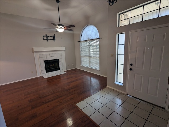 entrance foyer with high vaulted ceiling, wood-type flooring, a tiled fireplace, and ceiling fan