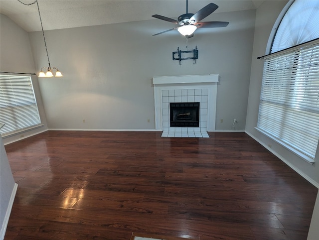 unfurnished living room with a healthy amount of sunlight, a tiled fireplace, ceiling fan with notable chandelier, and dark hardwood / wood-style floors