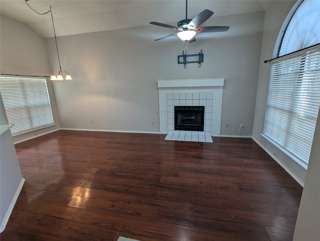 unfurnished living room featuring ceiling fan with notable chandelier, lofted ceiling, dark wood-type flooring, and a tile fireplace