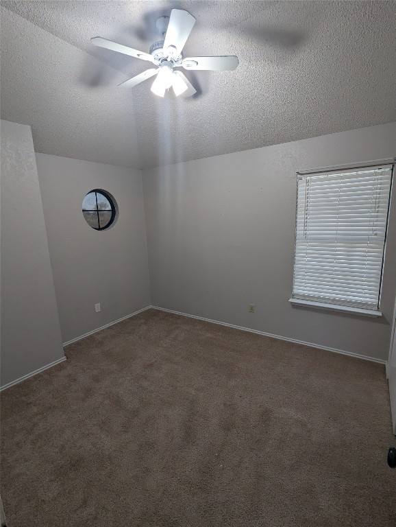 empty room featuring ceiling fan, a textured ceiling, lofted ceiling, and dark colored carpet