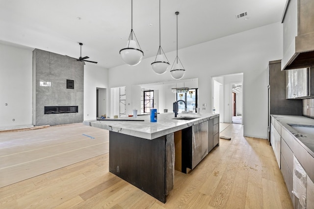 kitchen featuring ceiling fan, sink, decorative light fixtures, a large island with sink, and light hardwood / wood-style floors