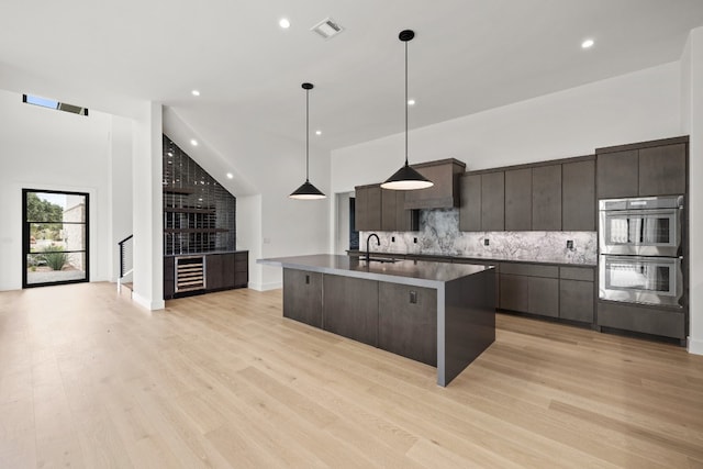 kitchen with stainless steel double oven, sink, dark brown cabinetry, pendant lighting, and light hardwood / wood-style floors