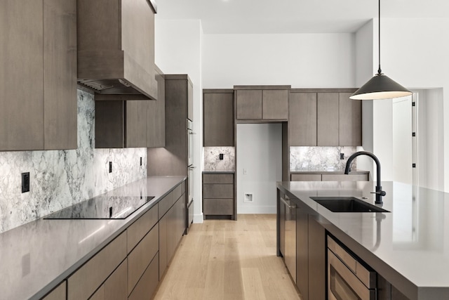 kitchen with black electric stovetop, sink, light wood-type flooring, wall chimney exhaust hood, and decorative light fixtures