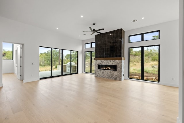 unfurnished living room with light hardwood / wood-style floors, a high ceiling, a fireplace, and ceiling fan