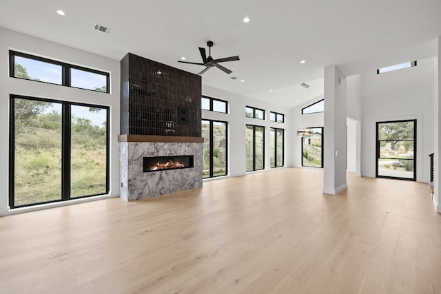 unfurnished living room with a high end fireplace, a high ceiling, light wood-type flooring, and ceiling fan