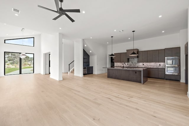 kitchen with dark brown cabinets, hanging light fixtures, light wood-type flooring, a high ceiling, and double oven