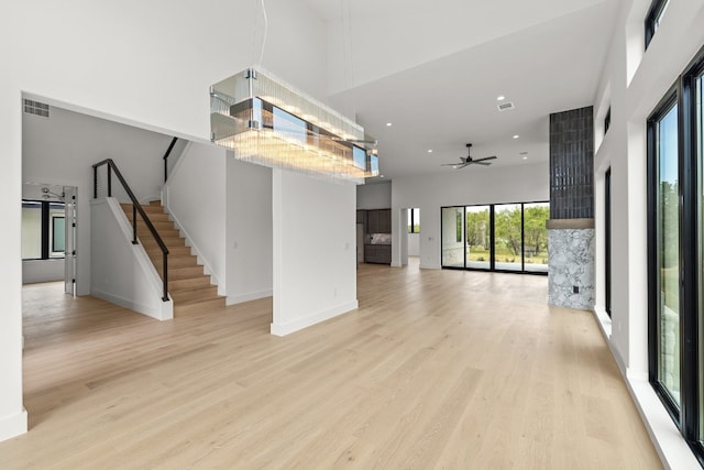 unfurnished living room with light hardwood / wood-style flooring, a high ceiling, and ceiling fan