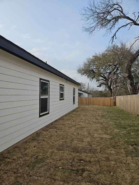 view of side of home with a lawn and fence