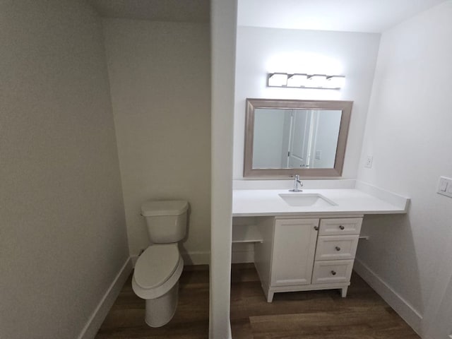 half bathroom with vanity, toilet, wood finished floors, and baseboards