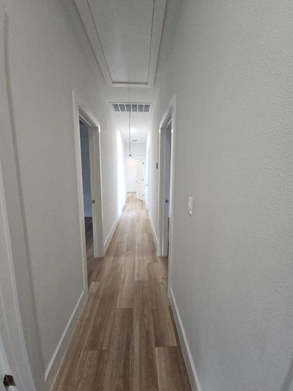 corridor featuring visible vents, attic access, baseboards, and wood finished floors