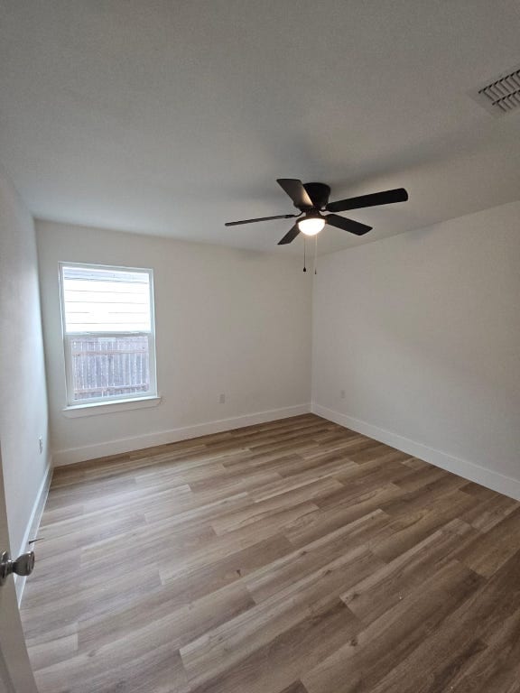 unfurnished room featuring a ceiling fan, visible vents, wood finished floors, and baseboards