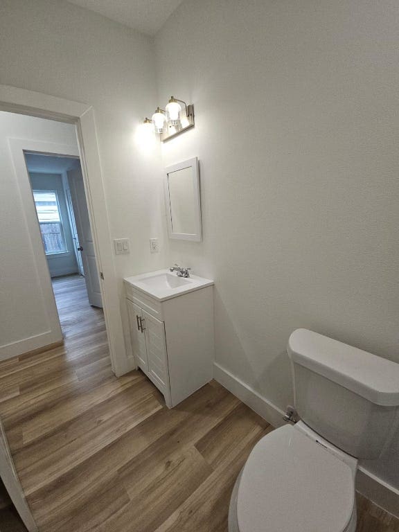 half bath with toilet, vanity, baseboards, and wood finished floors