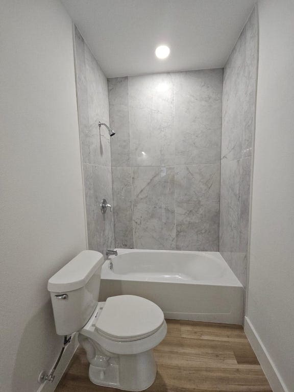 full bath featuring shower / tub combination, toilet, wood finished floors, and baseboards