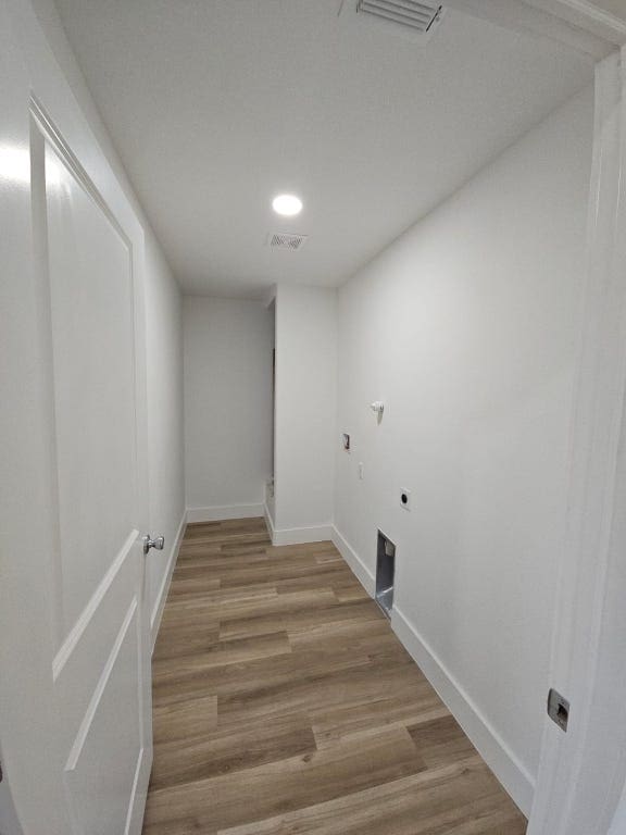 laundry area with electric dryer hookup, visible vents, wood finished floors, baseboards, and laundry area