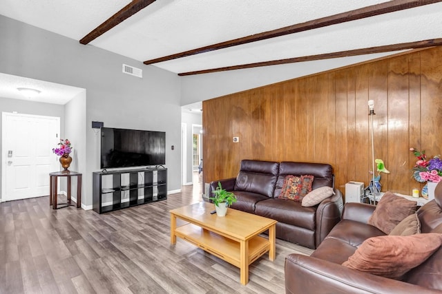 living room with vaulted ceiling with beams, wood walls, a textured ceiling, and hardwood / wood-style flooring