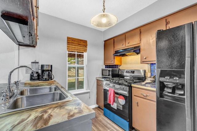 kitchen featuring light wood-type flooring, sink, hanging light fixtures, decorative backsplash, and stainless steel appliances